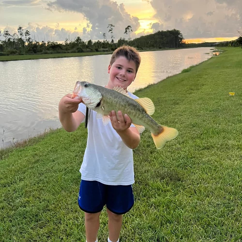 A young boy proudly holding a bass beside a WildBlue lake at sunset