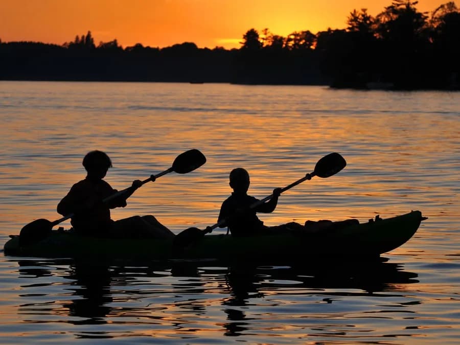 Two people paddling a tandem kayak across orange sunset reflections