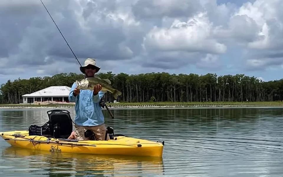 A male WildBlue resident holding a bass from a yellow kayak on the lake